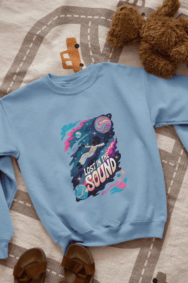 A baby blue white sweatshirt lying on the floor with the design of a man floating in space. There’s a text saying Lost in the Sound.