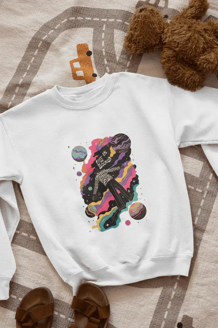 A printed white sweatshirt lying on the floor. The design of the sweatshirt contains of a man floating in space. The design is a colourful design with tiny planets and stars. There’s a text saying Lost in the sound.