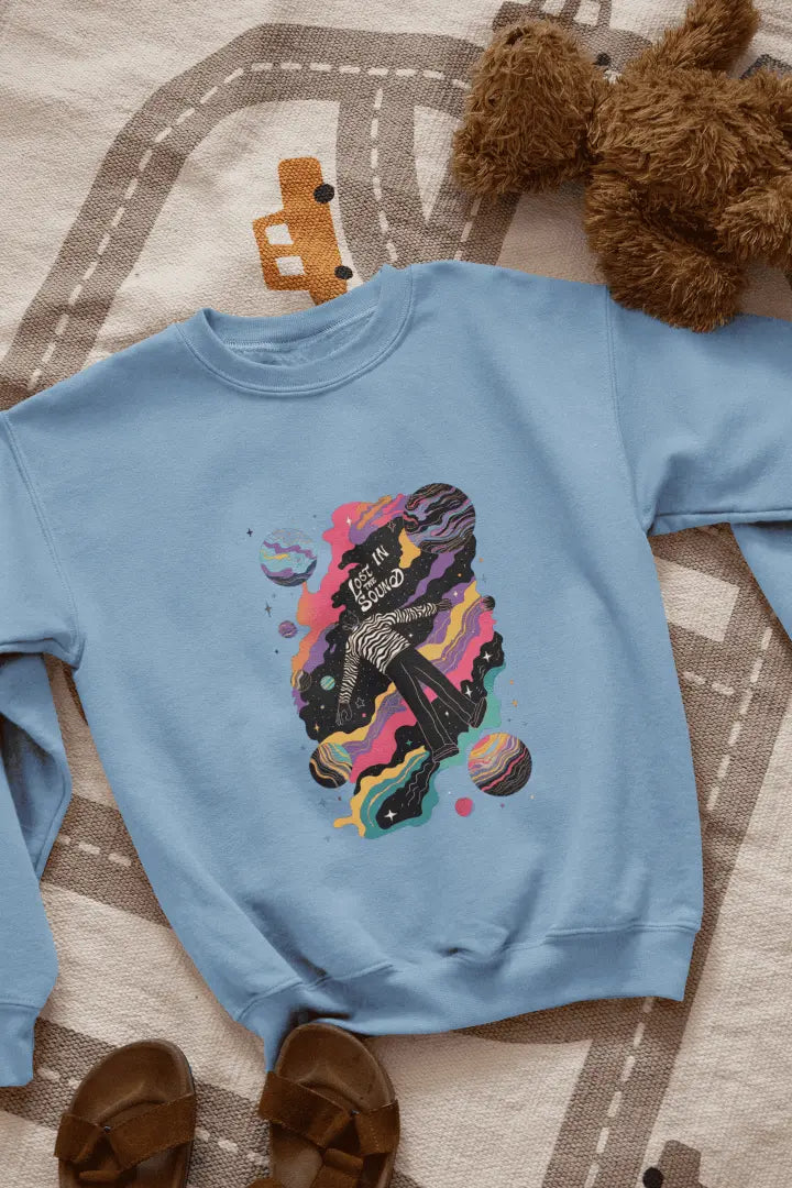 A printed baby blue sweatshirt lying on the floor. The design of the sweatshirt contains of a man floating in space. The design is a colourful design with tiny planets and stars. There’s a text saying Lost in the sound.