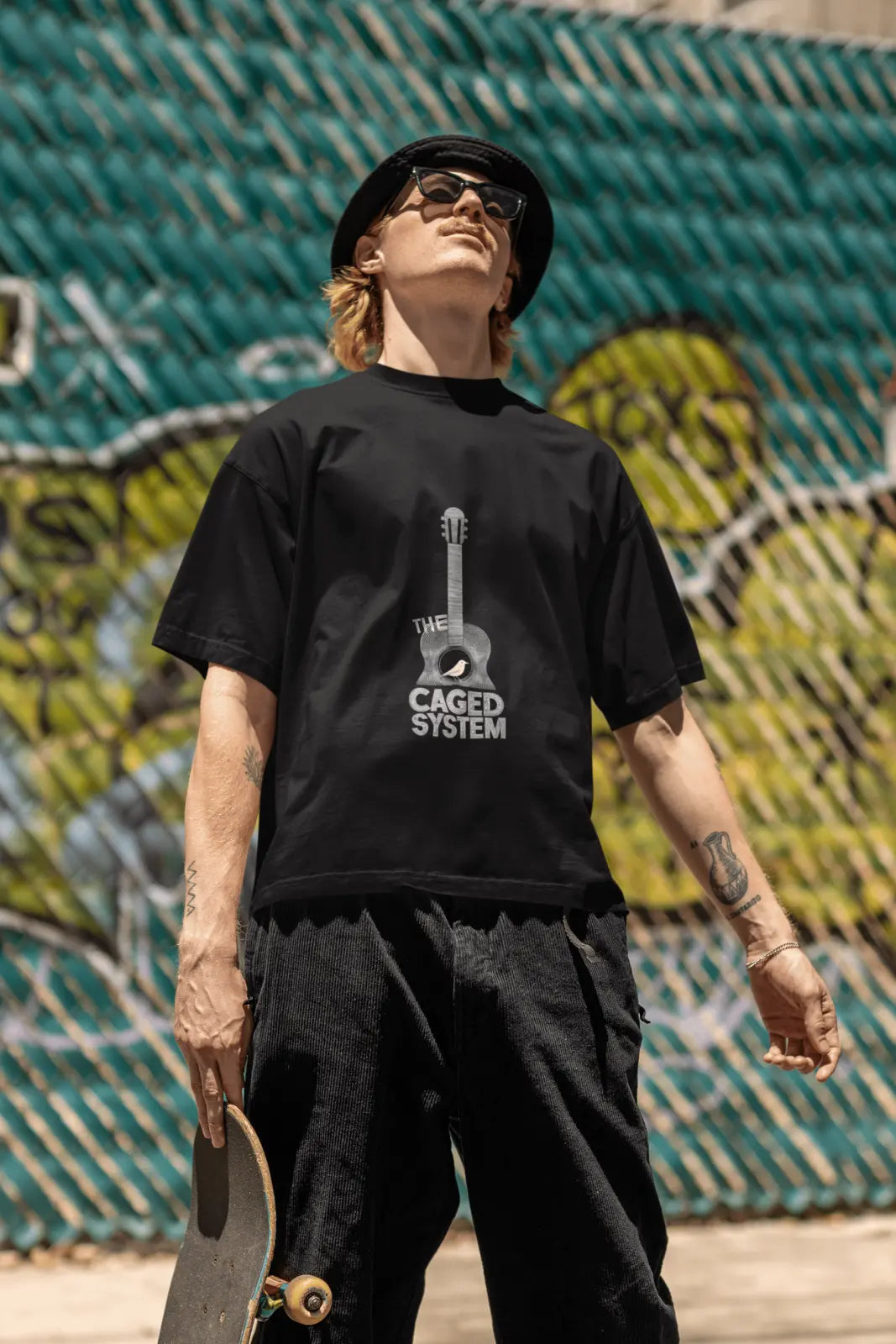 A man wearing a black printed 
oversized t-shirt with a minimal guitar design saying The Caged System.