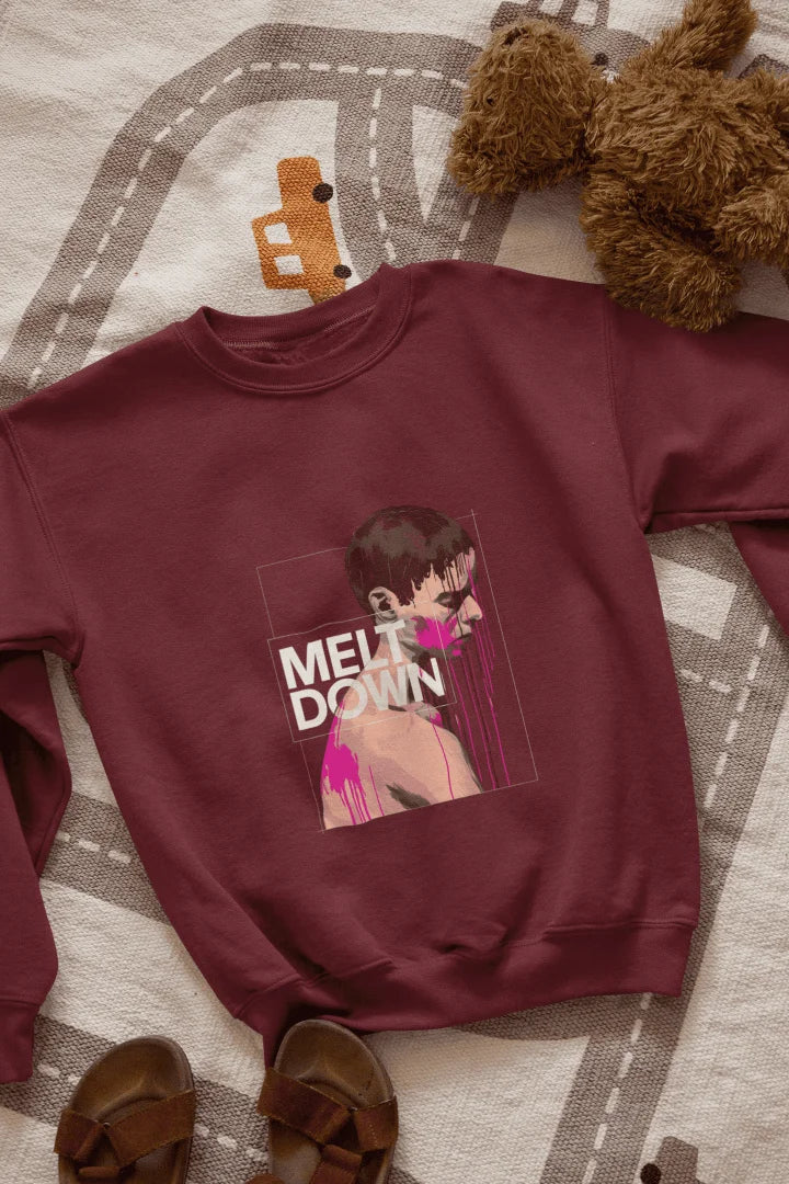 A maroon sweatshirt lying on the floor containing the design of a man in grief. The man is covered in pink paint splashes with paint dripping down from his face. There’s a text saying Meltdown on the design. 