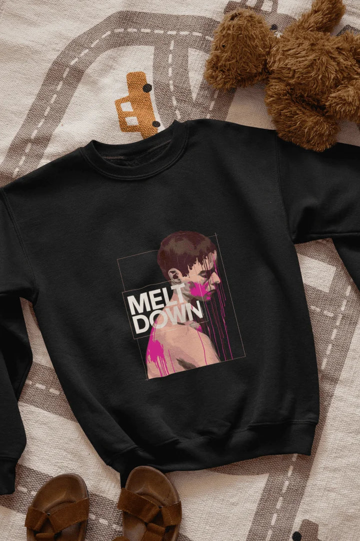 A black sweatshirt lying on the floor containing the design of a man in grief. The man is covered in pink paint splashes with paint dripping down from his face. There’s a text saying Meltdown on the design. 