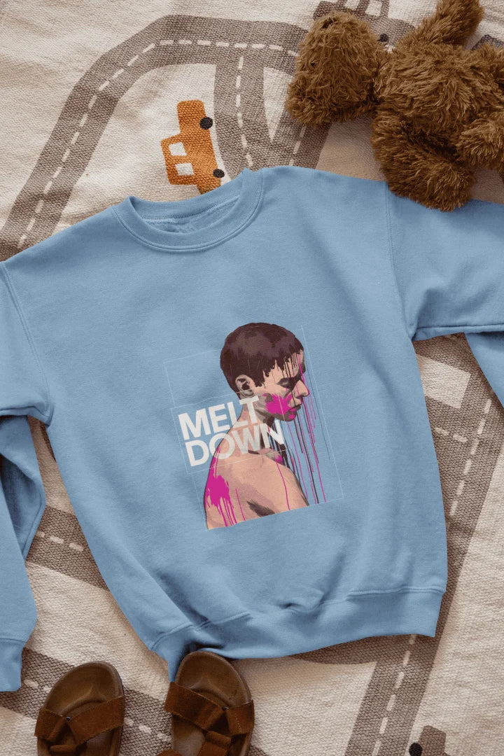 A baby blue sweatshirt lying on the floor containing the design of a man in grief. The man is covered in pink paint splashes with paint dripping down from his face. There’s a text saying Meltdown on the design. 
