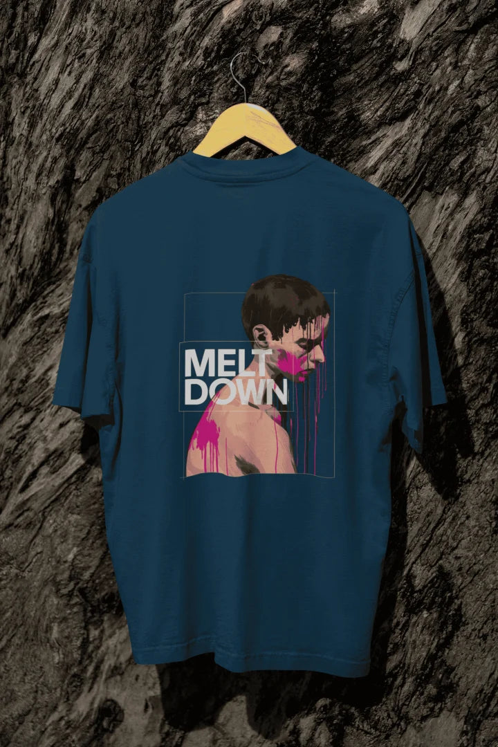 A navy blue oversized T-shirt hanging against a tree, containing the design of a man in grief. The man is covered in pink paint splashes with paint dripping down from his face. There’s a text saying Meltdown on the design. 