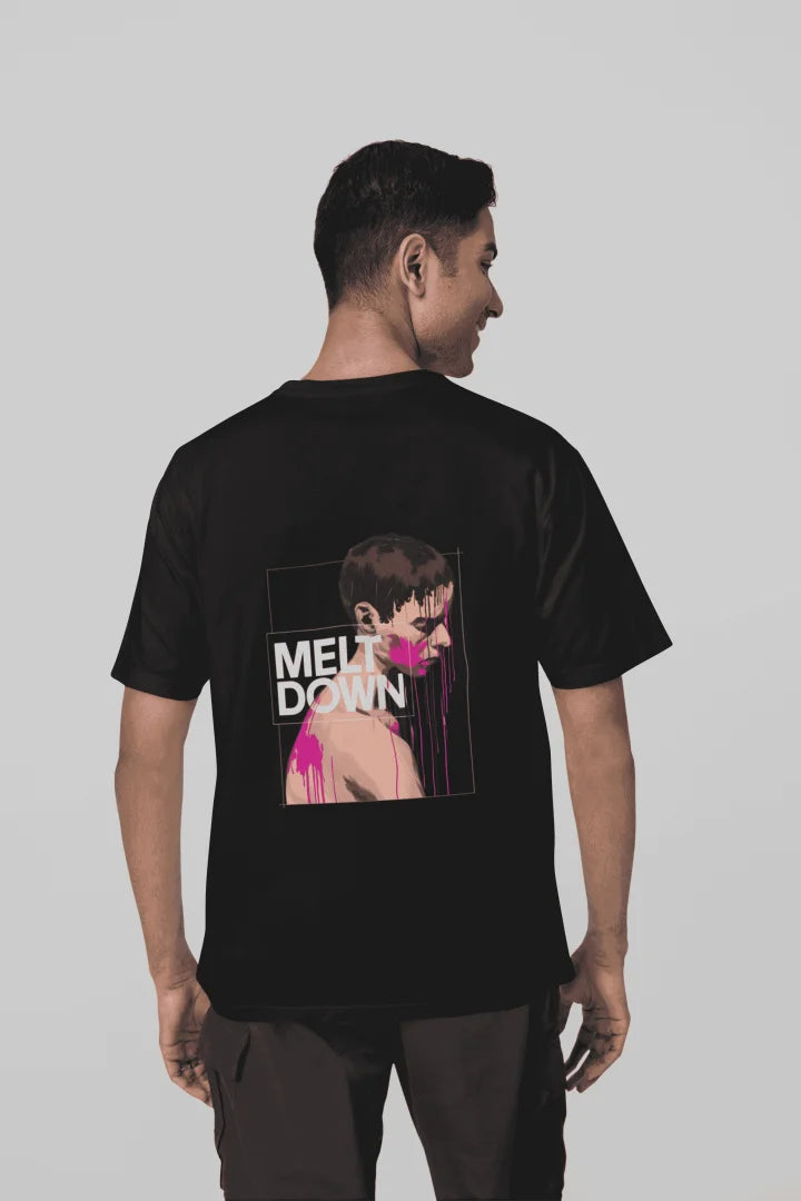A man wearing a black oversized T-shirt with a back print containing the design of a man in grief. The man is covered in pink paint splashes with paint dripping down from his face. There’s a text saying Meltdown on the design. 