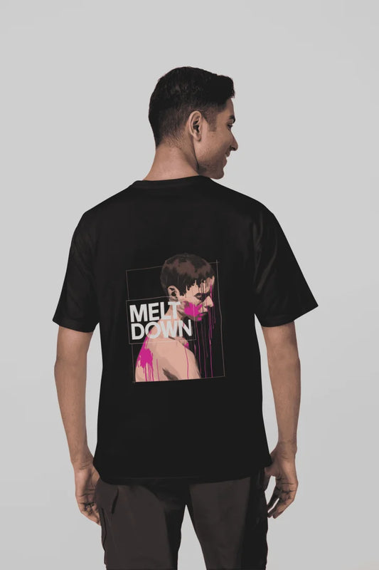 A man wearing a black oversized T-shirt with a back print containing the design of a man in grief. The man is covered in pink paint splashes with paint dripping down from his face. There’s a text saying Meltdown on the design. 