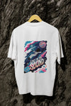 A white oversized t-shirt with a back print hanging on a tree trunk. The print design contains a kid floating in space with planets and starts surrounding him. There is a text saying Lost In The Sound on the design.