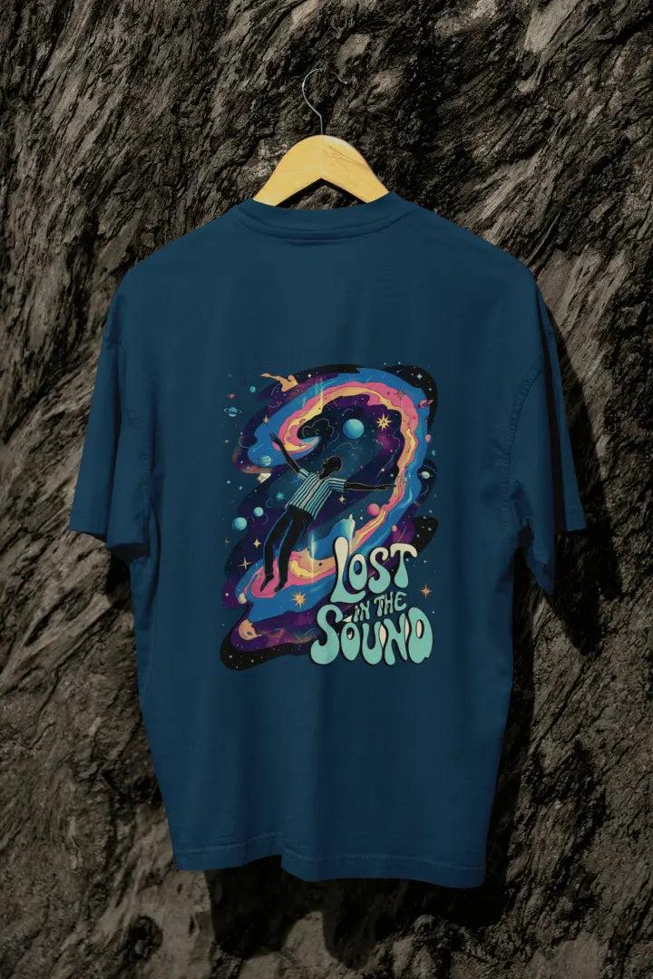 A navy blue back printed oversized t-shirt with a back print hanging on a tree trunk. The back print contains a man floating in space with planets and stars around him. There's a text saying Lost in The Sound on the bottom right of the design.