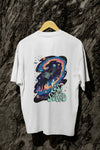 A white back printed oversized t-shirt with a back print hanging on a tree trunk. The back print contains a man floating in space with planets and stars around him. There's a text saying Lost in The Sound on the bottom right of the design.