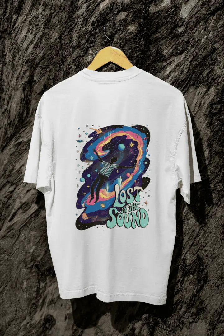 A white back printed oversized t-shirt with a back print hanging on a tree trunk. The back print contains a man floating in space with planets and stars around him. There's a text saying Lost in The Sound on the bottom right of the design.