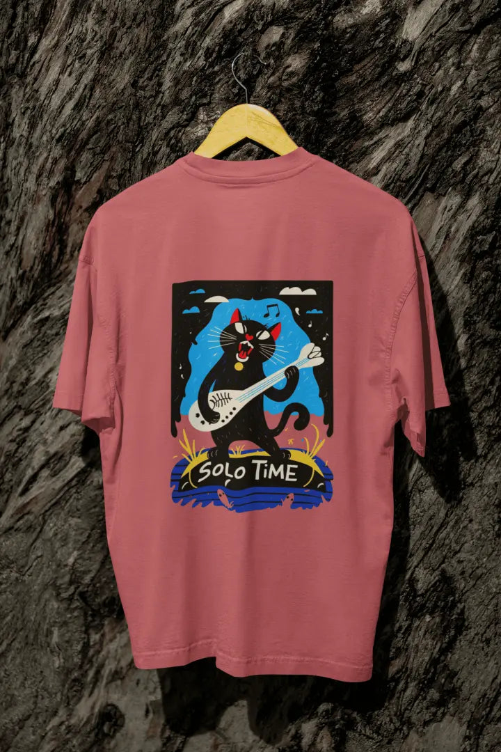 A dusty rose back printed oversized t-shirt with a back print hanging from a tree trunk. The design contains a cat holding a fish bone like a guitar and appears to play it aggressively. There's a text saying Solo Time at the bottom of the design.