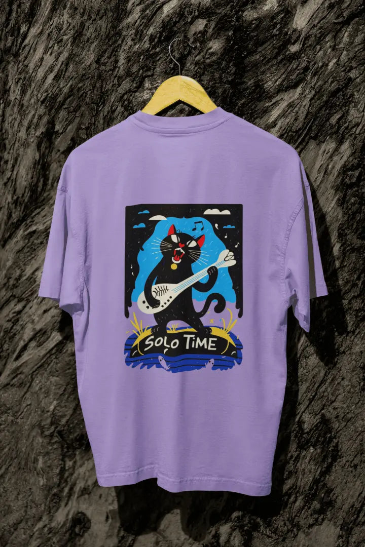 A lavender back printed oversized t-shirt with a back print hanging from a tree trunk. The design contains a cat holding a fish bone like a guitar and appears to play it aggressively. There's a text saying Solo Time at the bottom of the design.