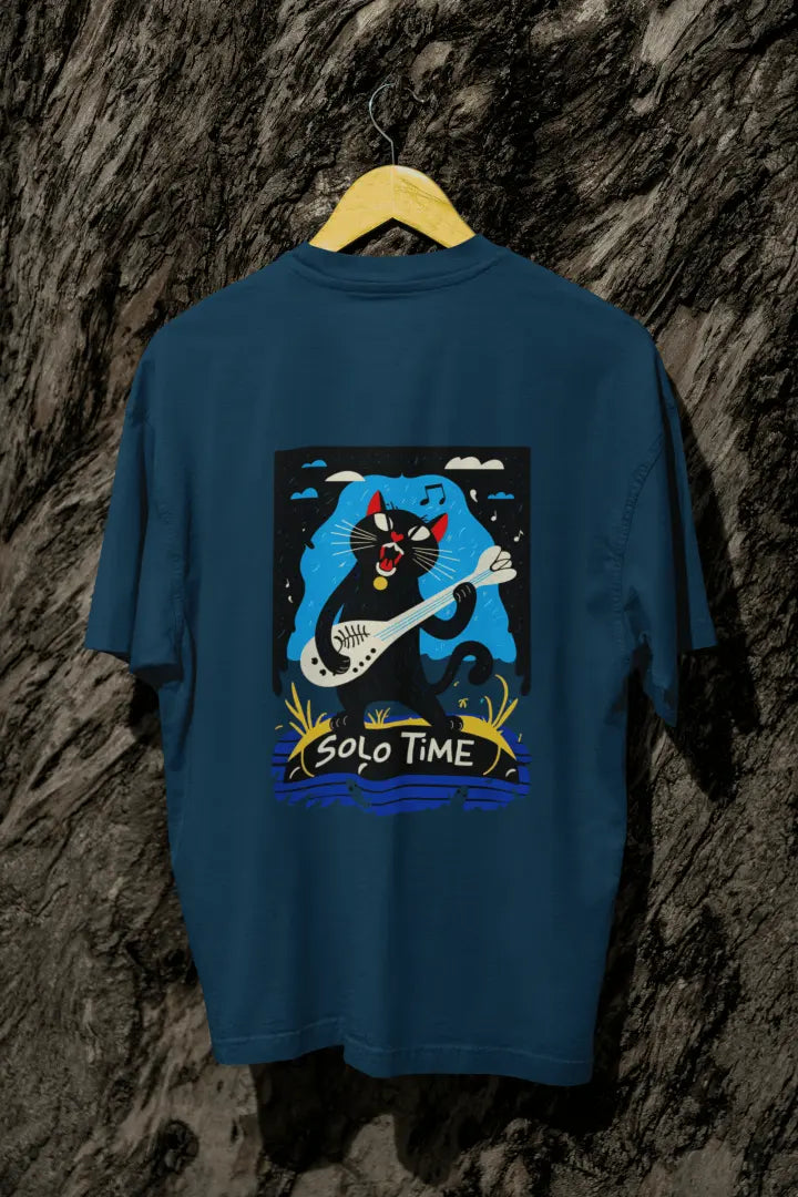 A navy blue back printed oversized t-shirt with a back print hanging from a tree trunk. The design contains a cat holding a fish bone like a guitar and appears to play it aggressively. There's a text saying Solo Time at the bottom of the design.
