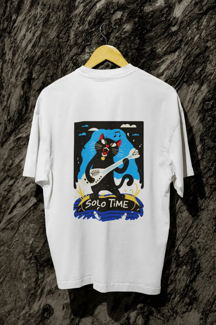 A white back printed oversized t-shirt with a back print hanging from a tree trunk. The design contains a cat holding a fish bone like a guitar and appears to play it aggressively. There's a text saying Solo Time at the bottom of the design.
