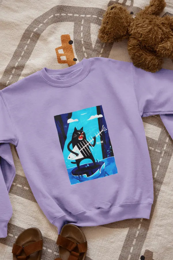 A lavender sweatshirt with a design printed on the front lying on the floor. The design contains a cat standing on an iceberg holding a fish bone which appears to be like a guitar. There's a text saying Solo Time on the right side.