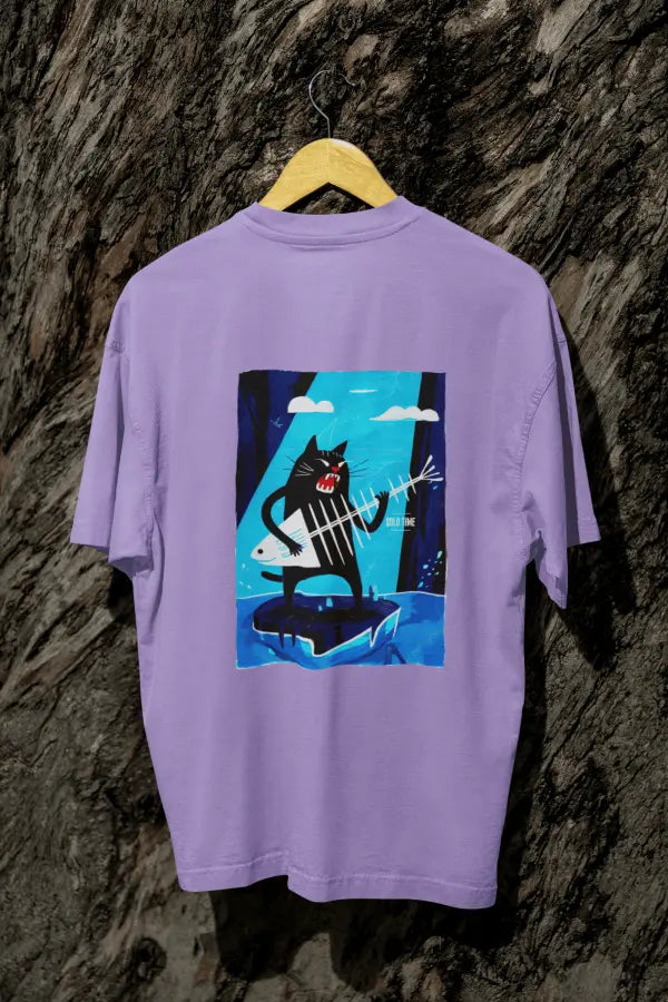 A lavender oversized t-shirt with a design printed on the back hanging against a tree trunk. The design contains a cat holding a fish bone like a guitar and appearing to play it aggressively. There's a text saying Solo Time on the right side of the design.