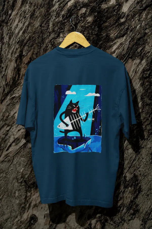 A navy blue oversized t-shirt with a design printed on the back hanging against a tree trunk. The design contains a cat holding a fish bone like a guitar and appearing to play it aggressively. There's a text saying Solo Time on the right side of the design.