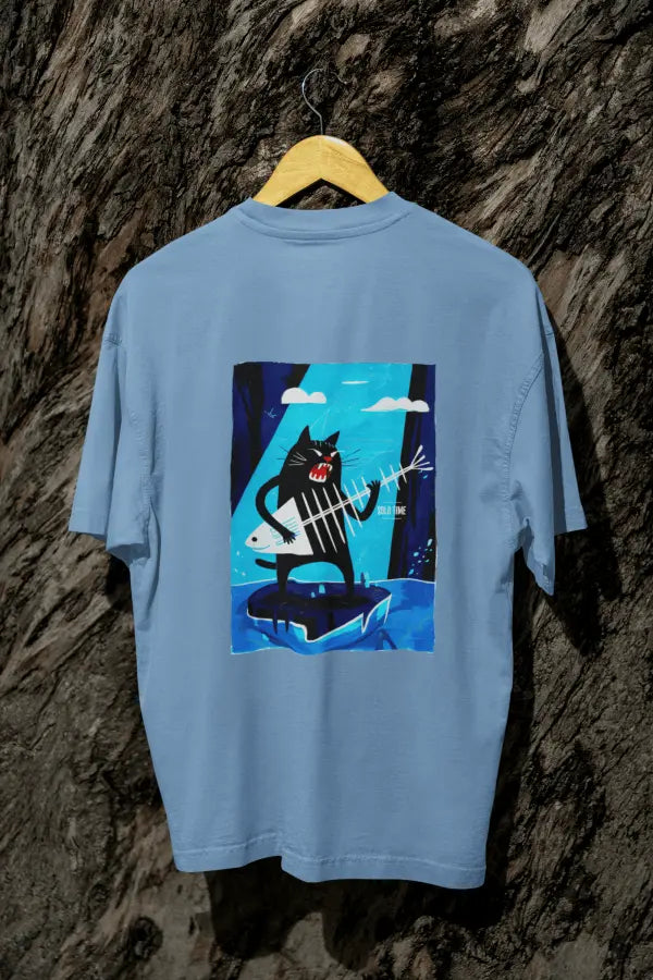 A baby blue oversized t-shirt with a design printed on the back hanging against a tree trunk. The design contains a cat holding a fish bone like a guitar and appearing to play it aggressively. There's a text saying Solo Time on the right side of the design.