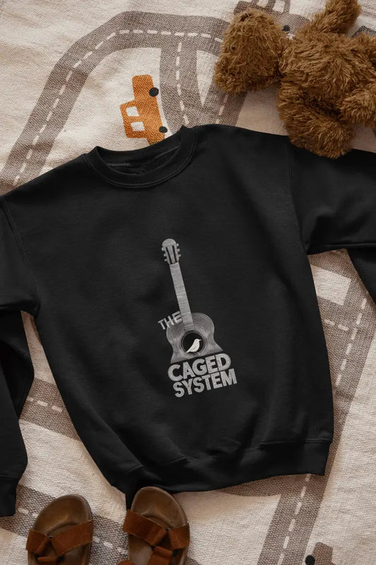 A black sweatshirt with a minimal design printed on the front lying on the floor. The design consists of an acoustic guitar inside which a small bird is sitting. There's a text saying The Caged System at the bottom of the design.