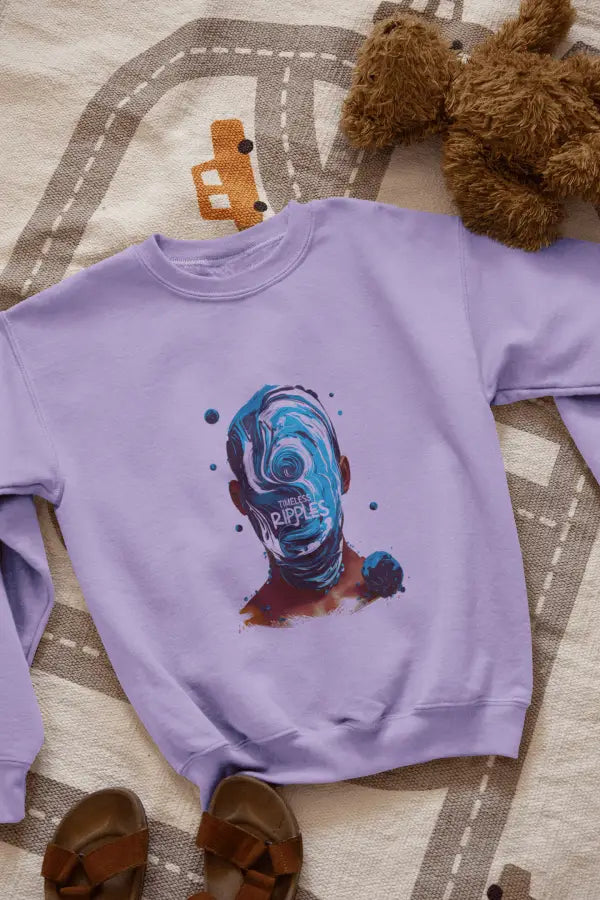 A lavender sweatshirt with a design printed on the front lying on the floor. The design contains a character whose face is made out of ripples of wave. There's a text saying Timeless Ripples at the center of the design.