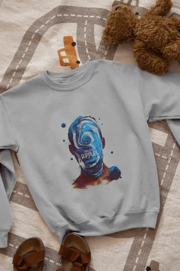 A grey sweatshirt with a design printed on the front lying on the floor. The design contains a character whose face is made out of ripples of wave. There's a text saying Timeless Ripples at the center of the design.